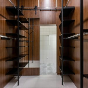 Empty black shelves and racks placed in modern walk in closet with brown walls and mirror with reflection at home